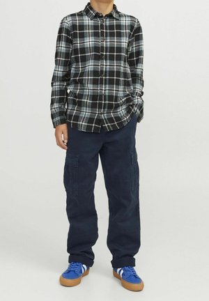 Carhart Flanellhemd mit Knopfleiste in schwarzem, blauem und weißem Karomuster, kombiniert mit blauen Cargohosen und blauen Sneakers. Lässiges, bequemes Design.