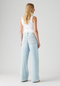 Lys blå vide jeans laget av denim, med baklommer og en liten logo-lapp. Kombinert med en tettsittende hvit tanktop.