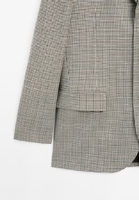 Giacca in tessuto houndstooth marrone e bianco, dal design strutturato, con una singola tasca sul davanti, realizzata in tessuto testurizzato.