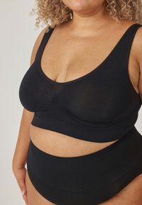 Czarny zestaw składający się z biustonosza i wysokich majtek wykonanych z gładkiej tkaniny. Biustonosz ma okrągły dekolt i szerokie ramiączka; majtki posiadają bezszwową konstrukcję.