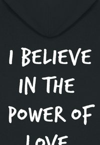 Črna jopa s kapuco z odebeljenim belim napisom: "VERJAMEM V MOČ LJUBEZNI." Mehka tkanina s sproščenim krojem in kapuco.