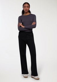 Szary długi rękaw, czarne spodnie szerokie u dołu i białe sneakersy z beżowymi podeszwami. Gładka tekstura i prosty design, odpowiednie na codzienne noszenie.