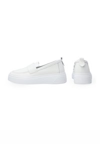Bílé slip-on boty s hladkým syntetickým svrškem, zaoblenou špičkou a plochou gumovou podrážkou. Obsahují zadní poutko pro snadné obouvání a minimalistische design.