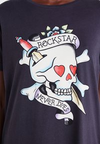 Juodas marškinėliai su dideliu kaukoles grafiku, raudonų širdžių, kryžminiais kaulais ir tatuiruotės stiliaus juostele su tekstu "ROCKSTAR NEVER DIES."