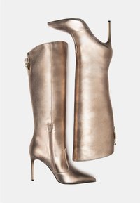 Bottes métalliques bronze jusqu'au genou avec un talon aiguille, un bout pointu, une fermeture éclair latérale et un ornement décoratif sur le dessus. Texture lisse.