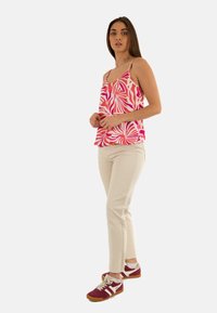 Top senza maniche rosa e bianco a fantasia con spalline sottili, abbinato a pantaloni beige chiaro e scarpe da ginnastica bordeaux.