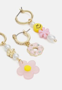 Brincos de argola dourados com encantos coloridos: uma cara sorridente amarela, uma flor rosa, um donut rosa com pedras preciosas e pérolas brancas.