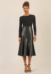 Schwarzer Leder-Midi-Rock mit ausgestelltem Schnitt, glatter Textur, hoher Taille und diagonaler Nahtdetails; kombiniert mit einem enganliegenden schwarzen Langarmoberteil.