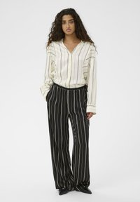 Črtasta bluzka v kremni in črni barvi z V-izrezom in dolgimi rokavi, v kombinaciji s širokimi hlačami s črtami v črni in beli barvi, ki imajo elastični pas.