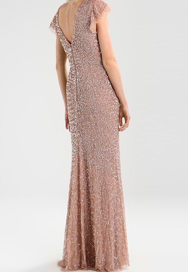 Langes, tailliertes Abendkleid in Blush mit einem V-Ausschnitt im Rücken, verziert mit Perlenstickerei, sanften Rüschensäumen und einem fließenden, strukturierten Rock.