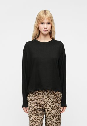 Top preto de mangas compridas com um corte descontraído, possui um decote redondo e uma textura suave, combinado com calças de estampado de leopardo.