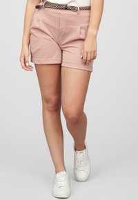 Lyserøde shorts med opbøjede kanter, to forlommer og et flettet brunt bælte. Kombineret med hvide sneakers for et afslappet look.