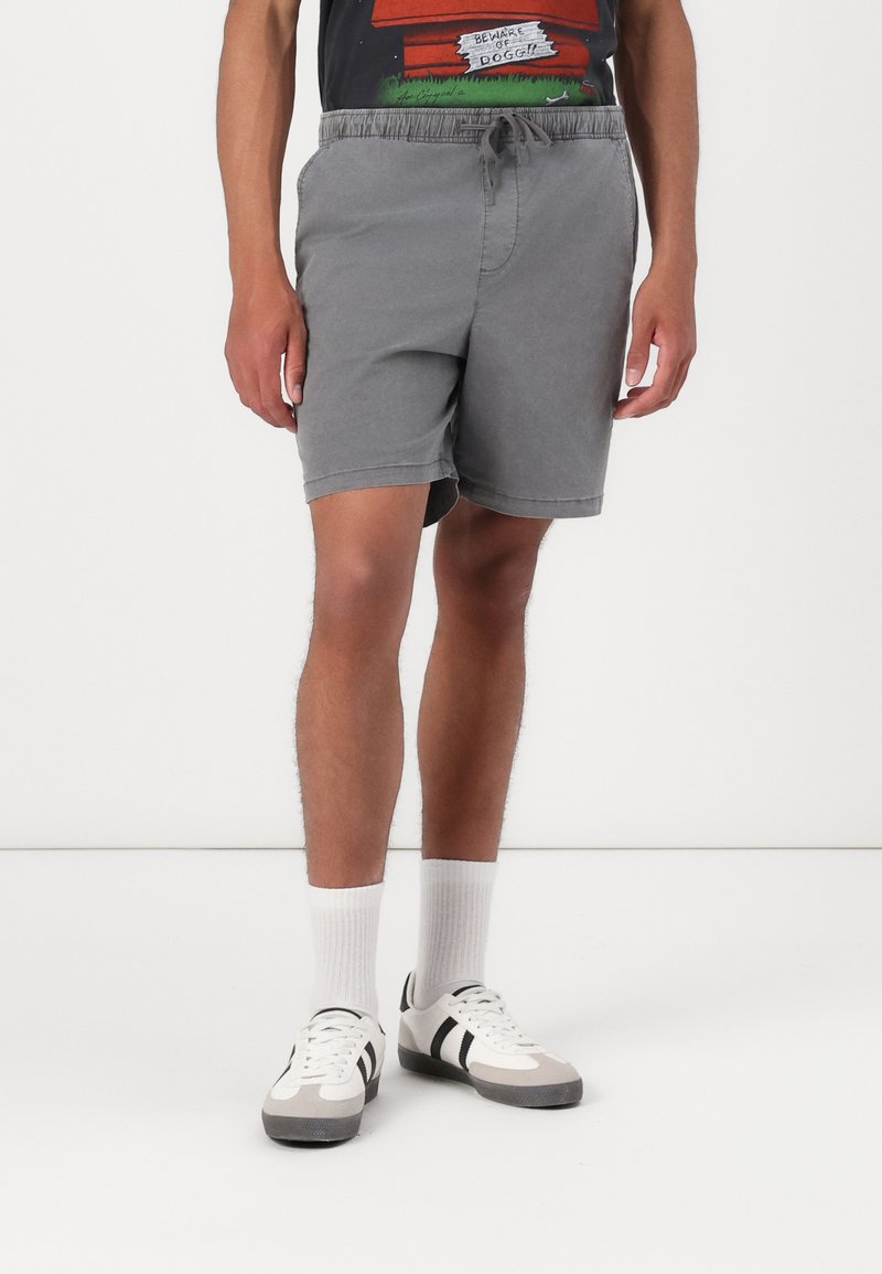 Shorts gris avec une taille élastique et un cordon de serrage. Présente une coupe décontractée et des poches latérales, associés à des chaussettes blanches et des chaussures décontractées.