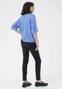 Top azzurro chiaro lavorato a maglia con motivo a diamante, maniche corte, orlo a coste, abbinato a pantaloni neri slim-fit e scarpe nere.