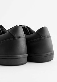 Czarne skórzane sneakersy o gładkiej fakturze, zaokrąglonym obcasie i minimalnych detalach szewnych. Solidna gumowa podeszwa z subtelnym wzorem bieżnika.