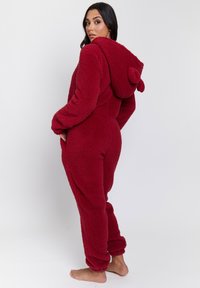 Mono de polar rojo con una superficie texturizada, que cuenta con una capucha con orejas y puños acanalados, diseñado para la comodidad y el calor.