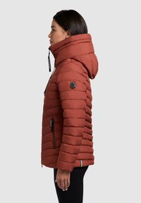 Rust-colored puffy jacket with horizontal quilting, high collar, adjustable hood, and black accents. Features zippered side pockets.