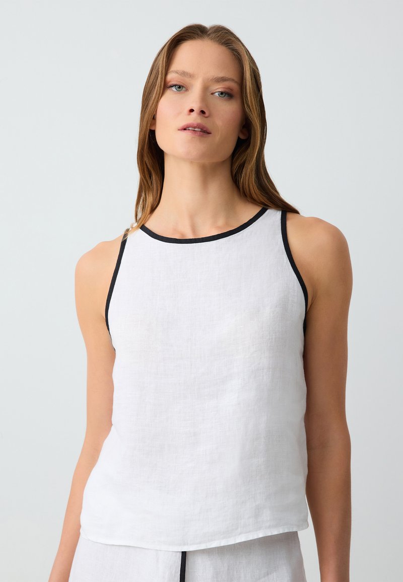 Débardeur en lin blanc avec bordures noires, présentant un encolure ronde et un design sans manches, légèrement ample, et une finition en tissu texturé.