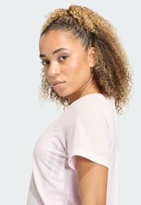 Jasnoróżowa sportowa koszulka z krótkimi rękawami i okrągłym dekoltem, cechująca się gładką fakturą i subtelnymi detalami wzorniczymi.
