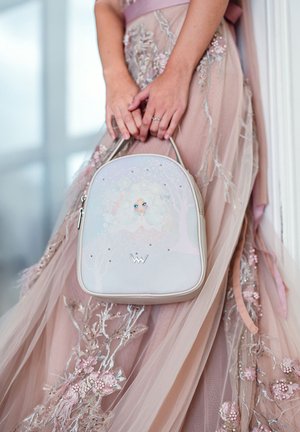 Weicher rosa Rucksack mit einer fantasievollen Illustration auf einer glatten, glänzenden Oberfläche. Akzentuiert mit kleinen silbernen Nieten und einem Logo.