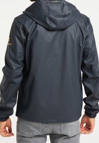 Veste imperméable bleu marine, texture lisse, avec capuche, poignets élastiques et détail de marque sur l'épaule. Design à la coupe décontractée.