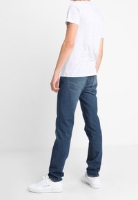 Tmavě modré džíny s přímým střihem, doplněné světle šedým tričkem a bílými teniskami. Jednoduchý design bez viditelných vzorů.