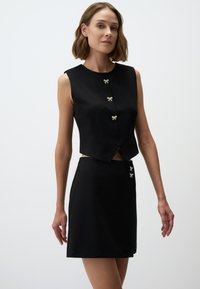 Completo due pezzi nero composto da un top senza maniche con bottoni a forma di fiocco e una mini gonna con dettagli in bottoni simili. Tessuto dal tocco liscio.