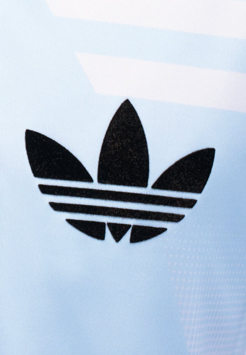 Schwarzes Adidas-Trefoil-Logo mit drei horizontalen Streifen auf hellblauem Stoffhintergrund.