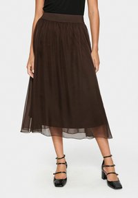 Bruine doorzichtige midi-rok met een elastische tailleband, met een vloeiendeontwerp en gelaagd stof. G gedragen met zwarte puntige hakken.