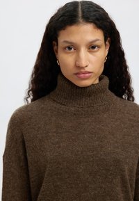 Barna garbó pulóver, puha, texturált anyagból; bordázott gallérral és laza szabással; minimalista dizájn minták vagy díszítések nélkül.