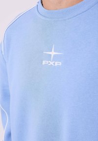 Lichtblauwe sweatshirt van zacht materiaal, met een ronde hals, witte accenten langs de schouders en een wit logo op de borst.