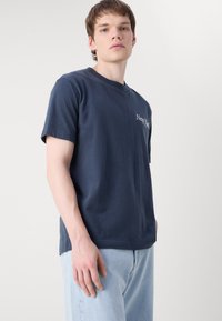 Navyblauwe katoenen t-shirt met korte mouwen, ronde halslijn en 'New York' tekstprint op de linkerkant van de borst. Casual fit met een soepele textuur.