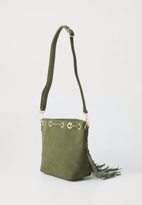 Borsa a secchiello verde in suede con hardware dorato, tracolla regolabile e dettaglio con nappine laterali. Presenta occhielli lungo la parte superiore per la chiusura.