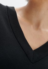 Pull noir à col en V avec un col côtelé et une texture douce, mettant en valeur des lignes épurées et une coupe ajustée.