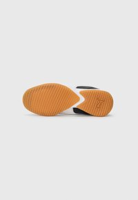 White sneaker with black accents shown from sole view, featuring orange textured rubber outsole and Puma logo on heel area.