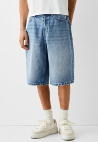 Ljusblå denimshorts med lös passform, knälång, med en klassisk femficksdesign och sydd kant, kombinerat med vita sneakers.