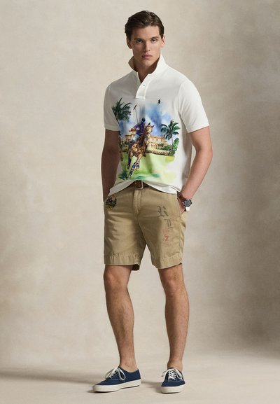 Balta polo krekls ar krāsainu polo ainu, haki šorti ar logotipiem un zili auduma apavi. Ir apkakle un brīvs piegriezums.