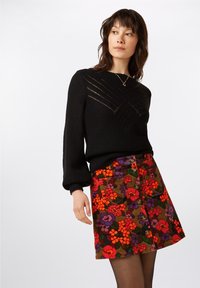 Sort strikket sweater med et struktureret diamantmønster på brystet, parret med en farverig blomster corduroy nederdel med knapdetaljer.