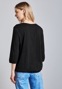 Schwarzes, langärmliges Oberteil mit Rundhalsausschnitt, lockerer Passform und glatter Textur, kombiniert mit hellblauen Denim-Jeans.