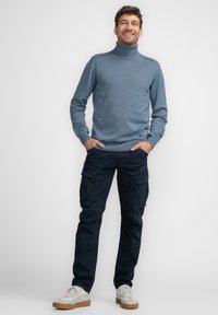 Lichtblauwe coltrui met ribbels aan de mouwen, gecombineerd met marineblauwe cargo broek met meerdere zakken, en witte sneakers met tan kleurige zolen.