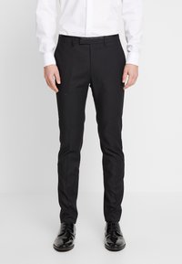 Svarta skräddarsydda byxor med en mjuk tygfinish, smal passform och subtila veck framtill, tillsammans med glänsande svarta kostymskor.