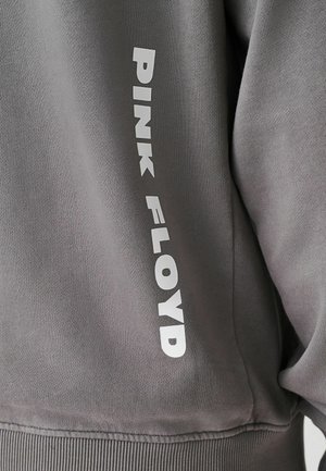 Harmaa huppari, jonka hihoissa on valkoista "PINK FLOYD" -tekstiä. Sileä rakenne ja ribatusta helma- ja hihansuun yksityiskohdista.