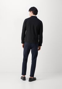 Μαύρο σακάκι με κουμπιά, μακριά μανίκια, συνδυασμένο με ναυτικές παντελόνες και μαύρα παπούτσια. Λείος ύφασμα, κομψή γραμμή, και rolled cuffs.