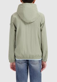 Lichtgroene hoodie-jack met een textuurafwerking, elastische manchetten en een elastische tailleband. Gecombineerd met blauwe jeans, wat een casual uitstraling geeft.