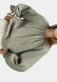Blusa a maniche lunghe, caratterizzata da una texture in verde tenue. Presenta un colletto arricciato e polsini elasticizzati, realizzata in un tessuto leggero e fluido.