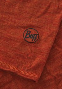 Chaussettes de cou en tissu extensible rouge avec une finition texturée et le logo circulaire noir "Buff". Couture visible le long du bord inférieur.