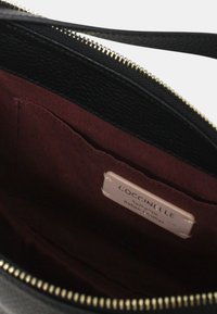 Borsa a mano in pelle nera con esterno testurizzato, zip dorata e fodera in tessuto bordeaux che mostra un'etichetta con le informazioni del marchio.
