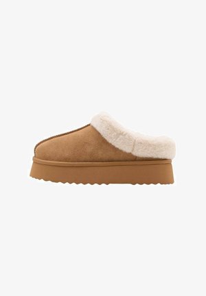 Zapatillas de casa tipo slip-on de ante marrón con un suave forro de piel sintética blanca y una suela de goma gruesa y texturizada, con un detalle de borde ondulado.