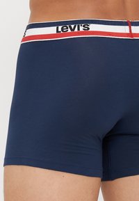 Μπλε ναυτικού ανδρικές μποξέρ με λαστιχένια μέση με επωνυμία και κόκκινες και λευκές ρίγες. Μαλακό ύφασμα, εφαρμοστή σχεδίαση και χωρίς ορατά σχέδια.