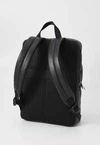 Mochila negra con materiales de cuero y malla, que cuenta con correas ajustables, un asa superior y un cierre con cremallera. Detalle de superficie texturizada.